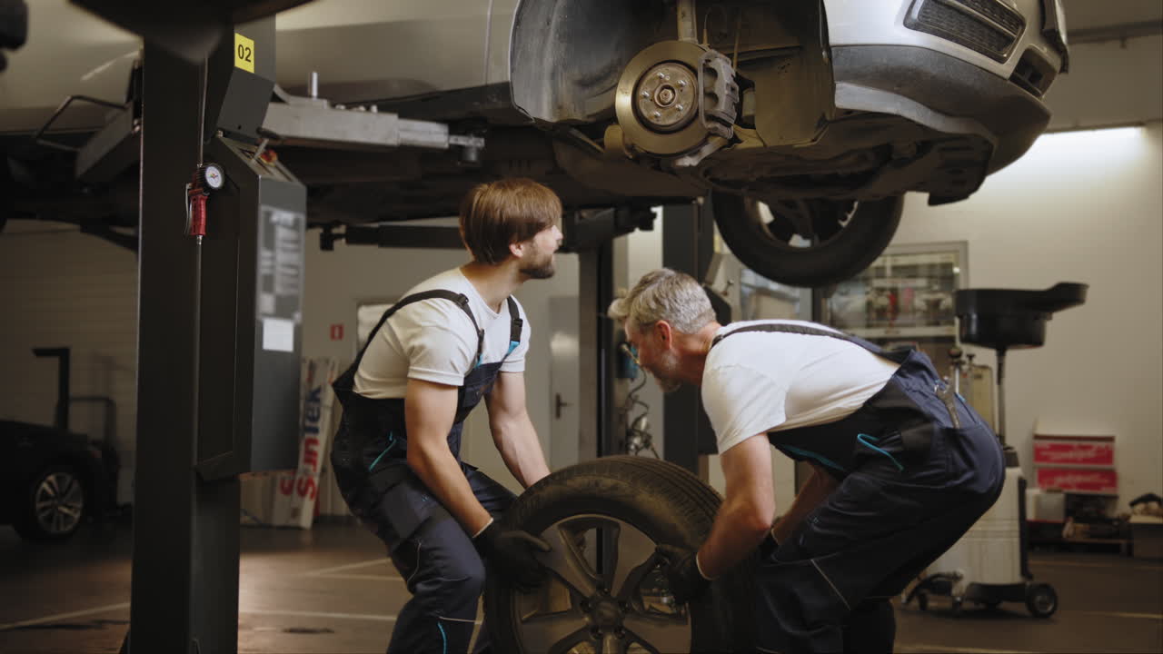 dos mecánicos cambiando un neumático en un ascensor de automóvil