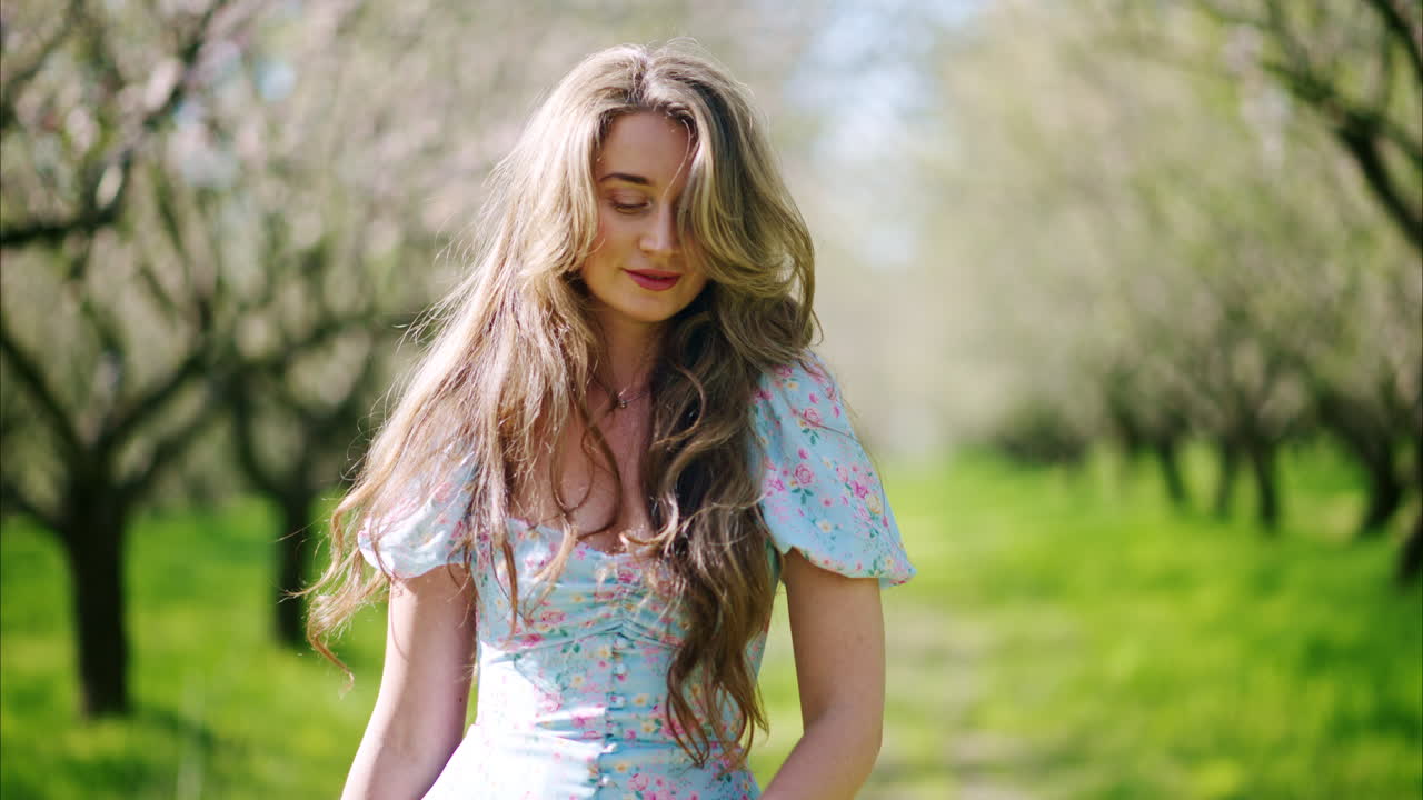 Brunette woman in a blue dress enjoying a field of blooming almond trees