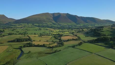 patchwork green fields and stream with flight towards mountains on sunny summer morning in the english lake district, cumbria, uk