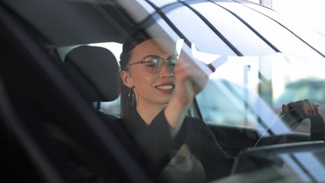 a woman is cleaning the vehicle windshield while seated in the car. a woman is cleaning the windshield of a vehicle, ensuring clear vision while seated inside the car. automotive design and exterior care are important for maintaining a safe driving environment