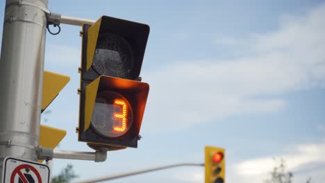 Pedestrian-crosswalk-light-on-metal-pole-at-traffic-intersection-with-traffic-lights-in-background-counting-down-under-bright-skies