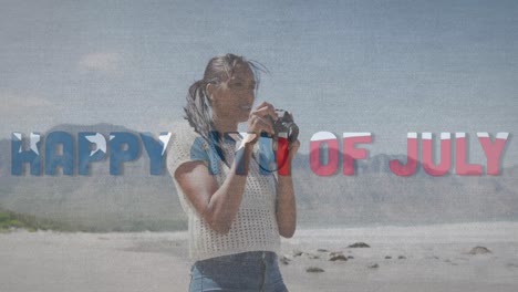 Animation-of-text-independence-day-over-african-american-woman-taking-photo-at-beach