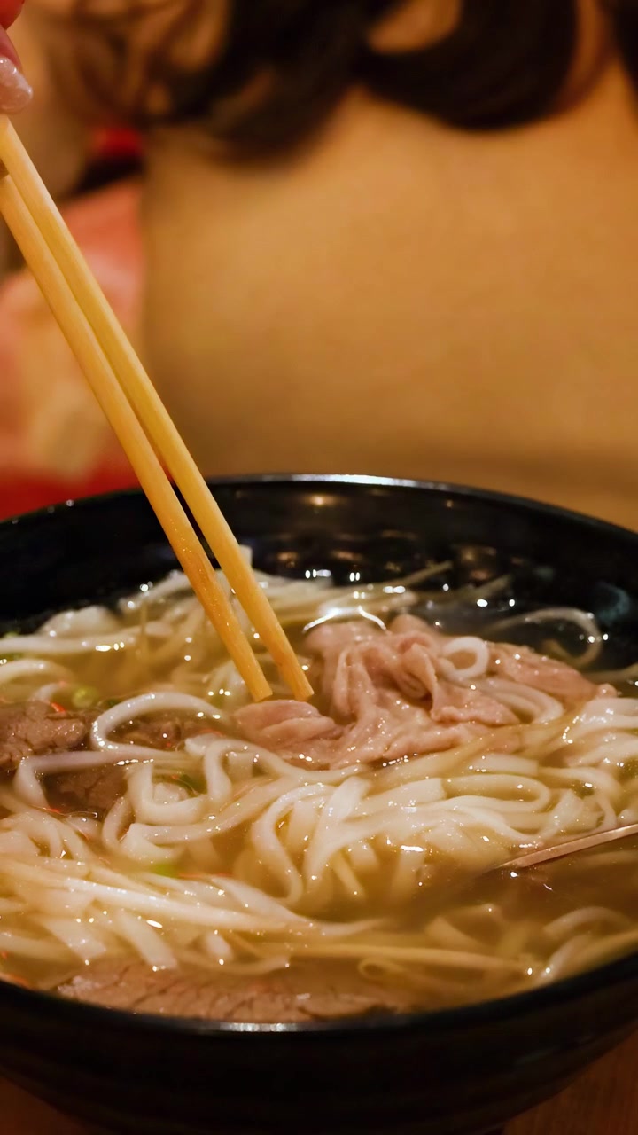 Una persona usa le bacchette per assaporare il pho vietnamita in un ambiente accogliente, evidenziando le ricche consistenze e i sapori del piatto.