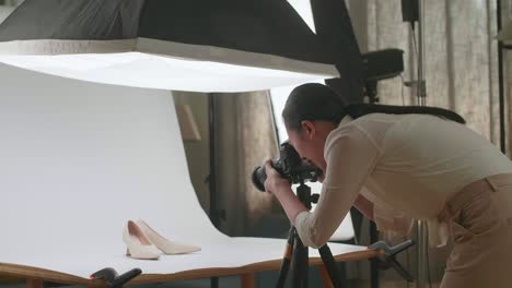 asian female photographer checking the photos of women's shoes after taking them in home studio