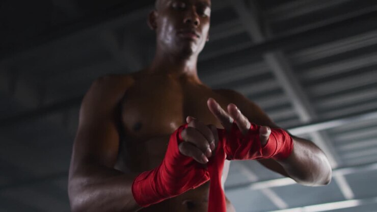 Uomo afroamericano a petto nudo che si fascia le mani per la boxe in un edificio urbano vuoto.