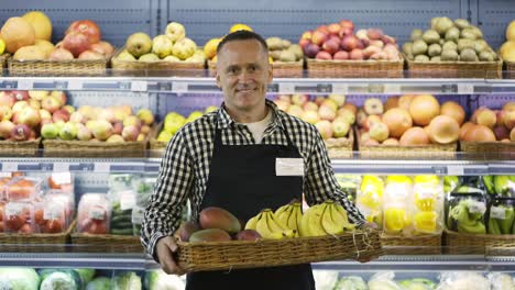 portrait of a happy middle-aged store worker holding a box of exotic fruits. a man in an apron and with a badge. shop working