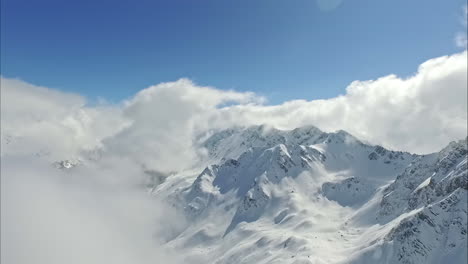 aerial view overlooking a mountain range with winter snow top peaks and low clouds forming against a blue background sky