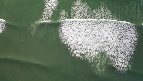 unique top down drone shot of waves crashing on beach