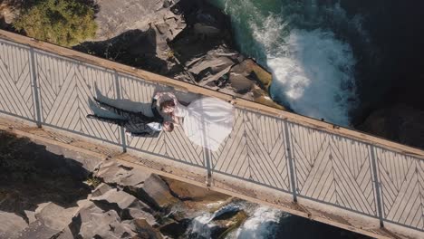 newlyweds. bride and groom lie on a bridge over a mountain river. aerial view