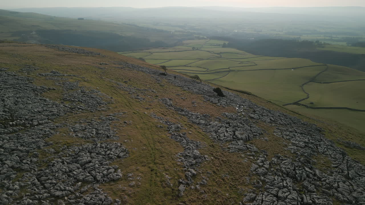 잉글턴 요크셔 영국의 패치워크 그린 필드와 안개 낀 지평선이 있는 바위 언덕에 있는 먼 하이커