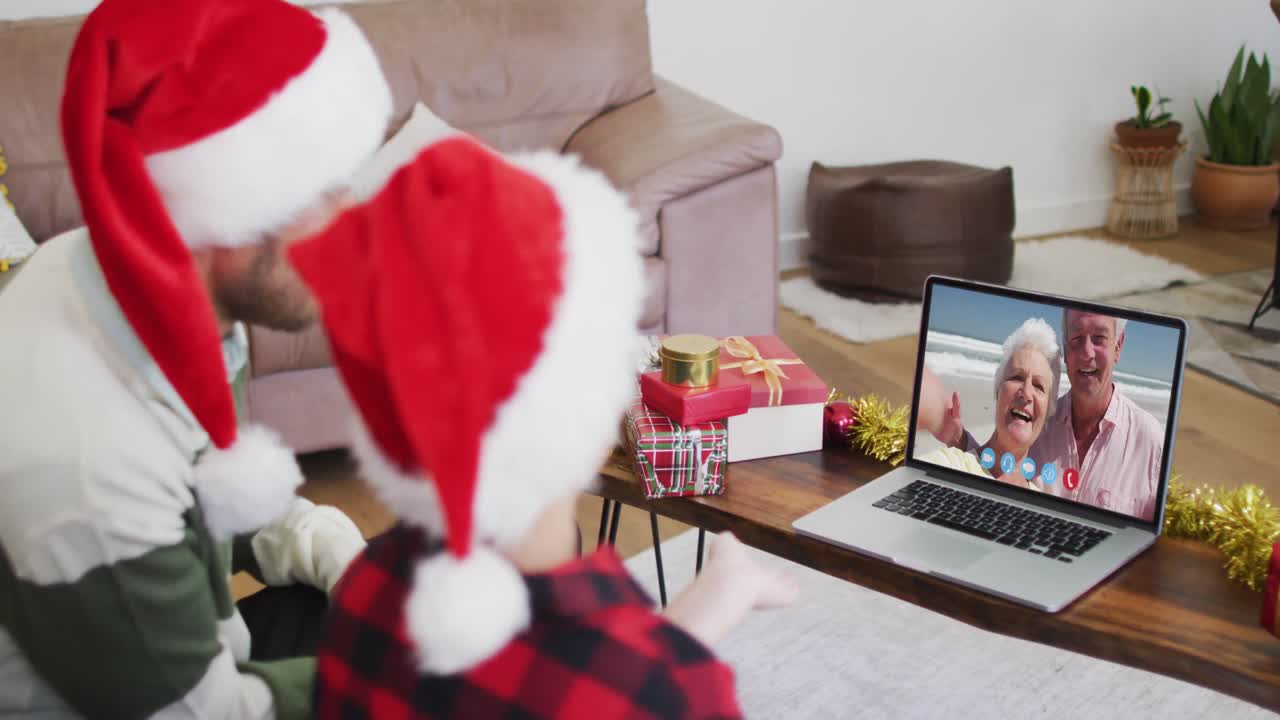 padre y hijo caucásicos usando sombreros de santa en una videochat portátil durante la navidad en casa