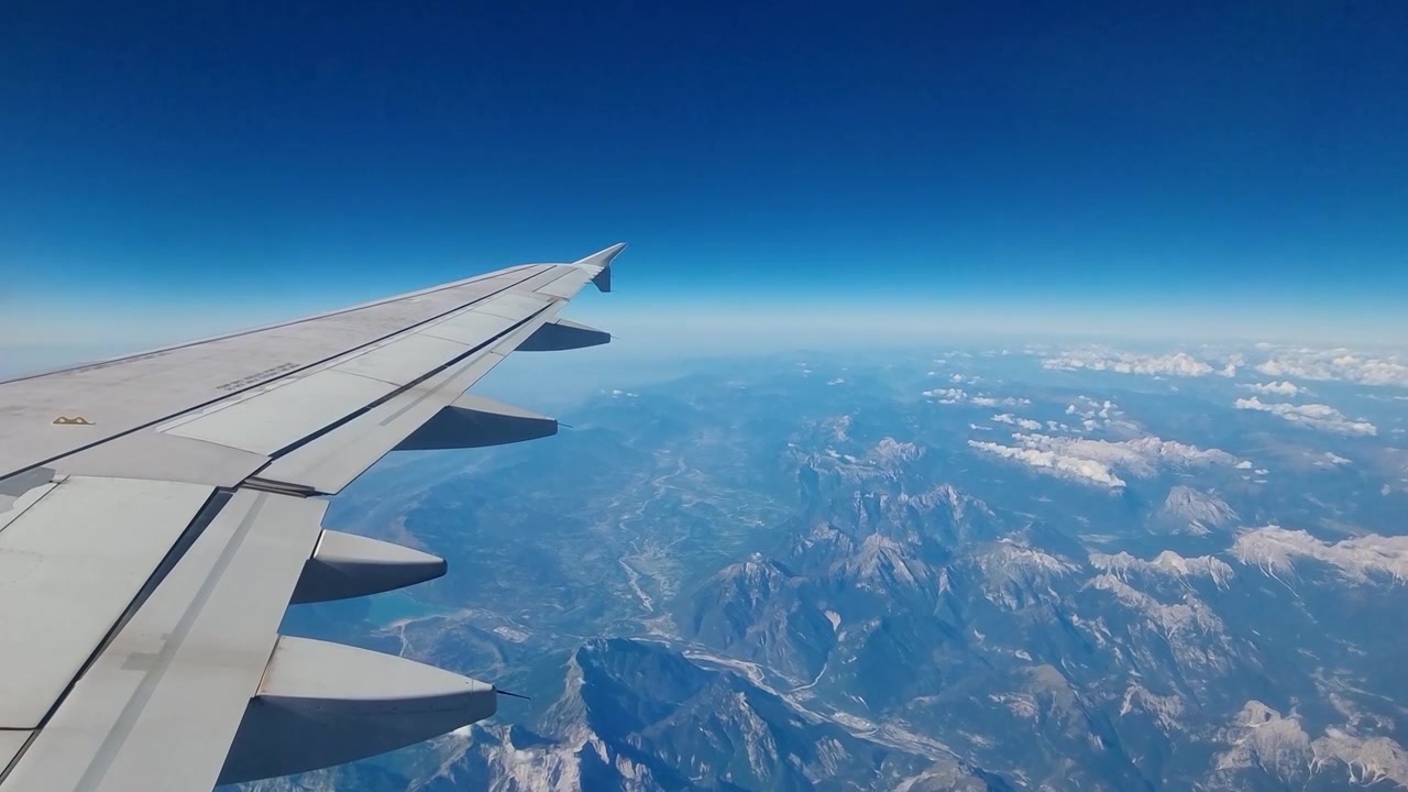 Vista dal finestrino di un aereo sull'ala del velivolo in volo sopra la Terra, con la curvatura del pianeta visibile sotto un cielo blu infinito, che evoca aviazione, viaggi aerei, libertà e un senso di prospettiva