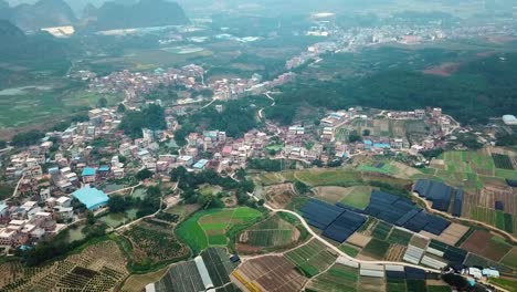 toma aérea de tierras de cultivo y aldea con pequeños picos irregulares en el fondo, granja de frutas de dragón en el condado de long&#39;an, guangxi, china