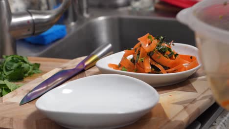 orange colored pasta noodles infused with tomato paste, carrots or chickpeas are decoratively plated in bowls while wearing blue rubber gloves on chef’s hands, closeup in restaurant or home kitchen