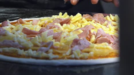 primer plano de la mano topping pizza con jamón y queso