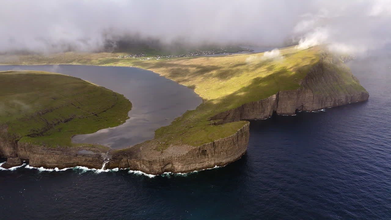 Aerial view of Lake Sørvágsvatn cliffs, Faroe Islands, with dramatic coastline, rolling clouds, rugged green slopes, and the Atlantic Ocean horizon, iconic Nordic landscape