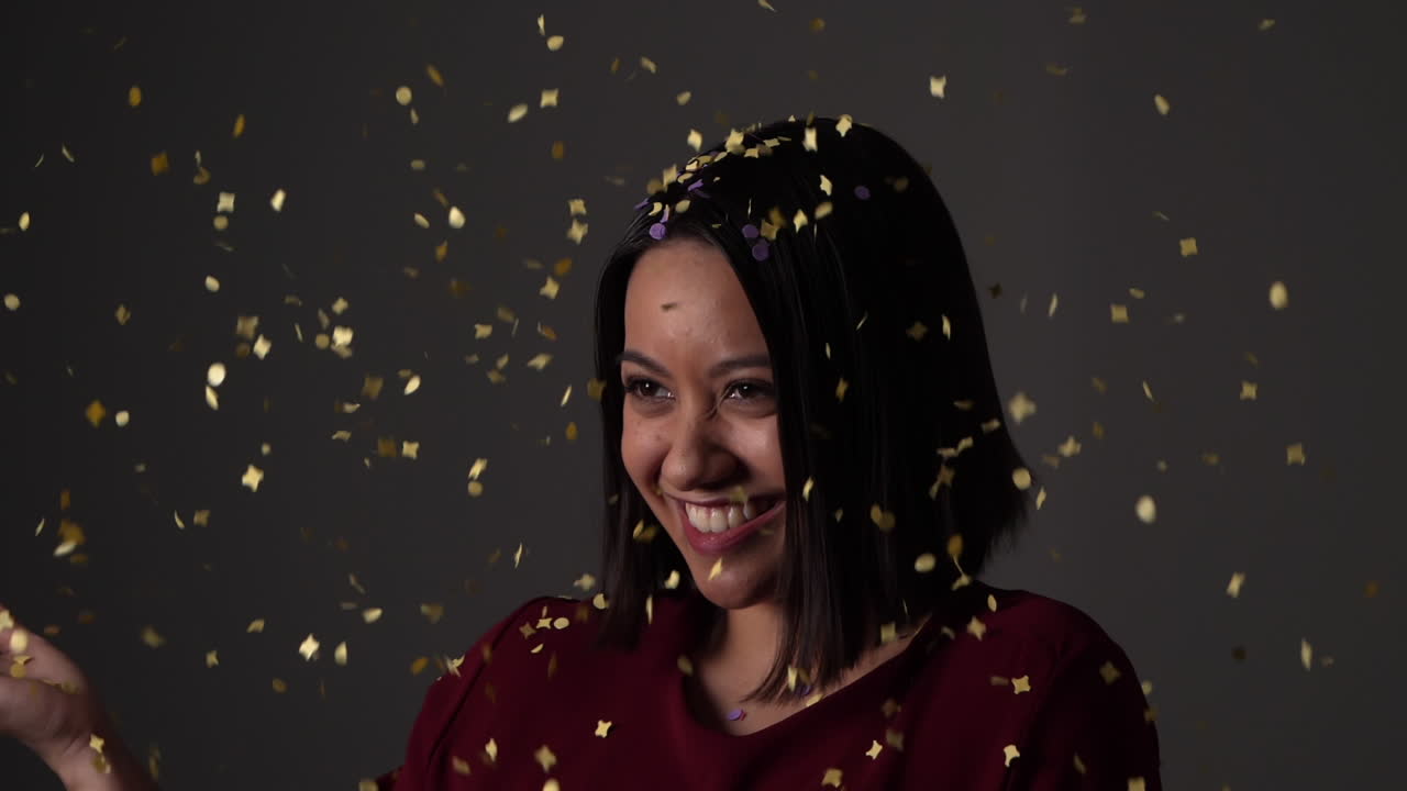 Jeune femme souriant doucement tout en recevant une pluie de confettis dorés - Ralenti.