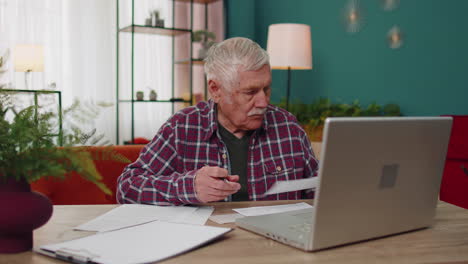 Serious-grandfather-man-calculating-household-bills-bank-loan-online-domestic-expenditures-payment