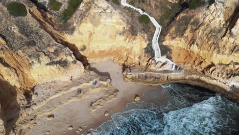 downhill path through rocky cliff to paradise beach, in carvoeiro, algarve, portugal - aerial push out low angle reveal shot