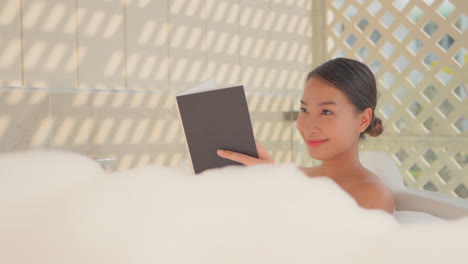 bella chica sonriendo mientras lee un libro sobre una bañera de lujo