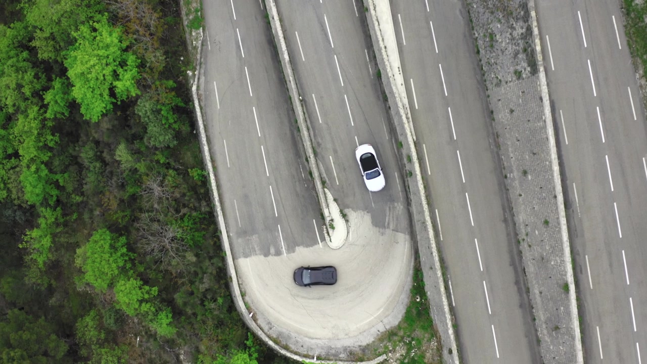 Auto sportiva Bentley che insegue una Lamborghini Huracan tra le curve su una strada tortuosa delle Alpi con drone