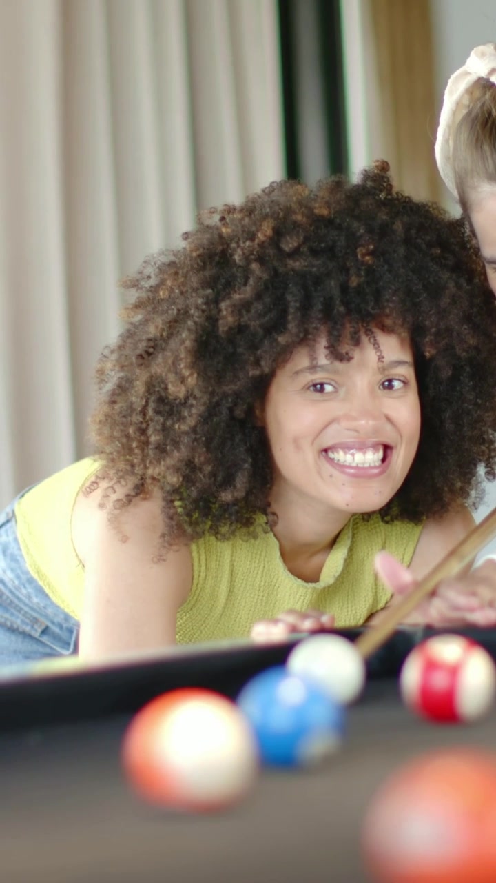 Vertical video: Leaning curly woman in lime lining up shot at pool table, cue and balls prompt play