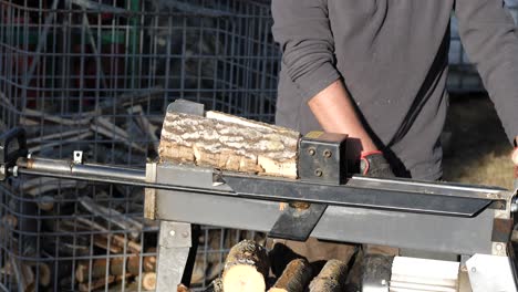 man using log cutting machine to chop wood, throwing firewood in a pile, rack focus