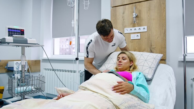 Caring loving husband stands at the head of his wife in hospital bed. Man calms down his pregnant spouse suffering from painful contractions.