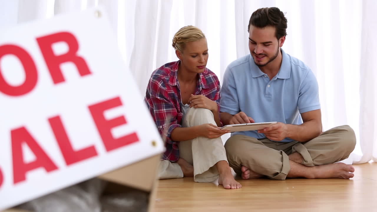 una pareja encantada sentada en el suelo usando una tableta