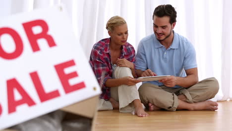 Delighted-couple-sitting-on-floor-using-tablet