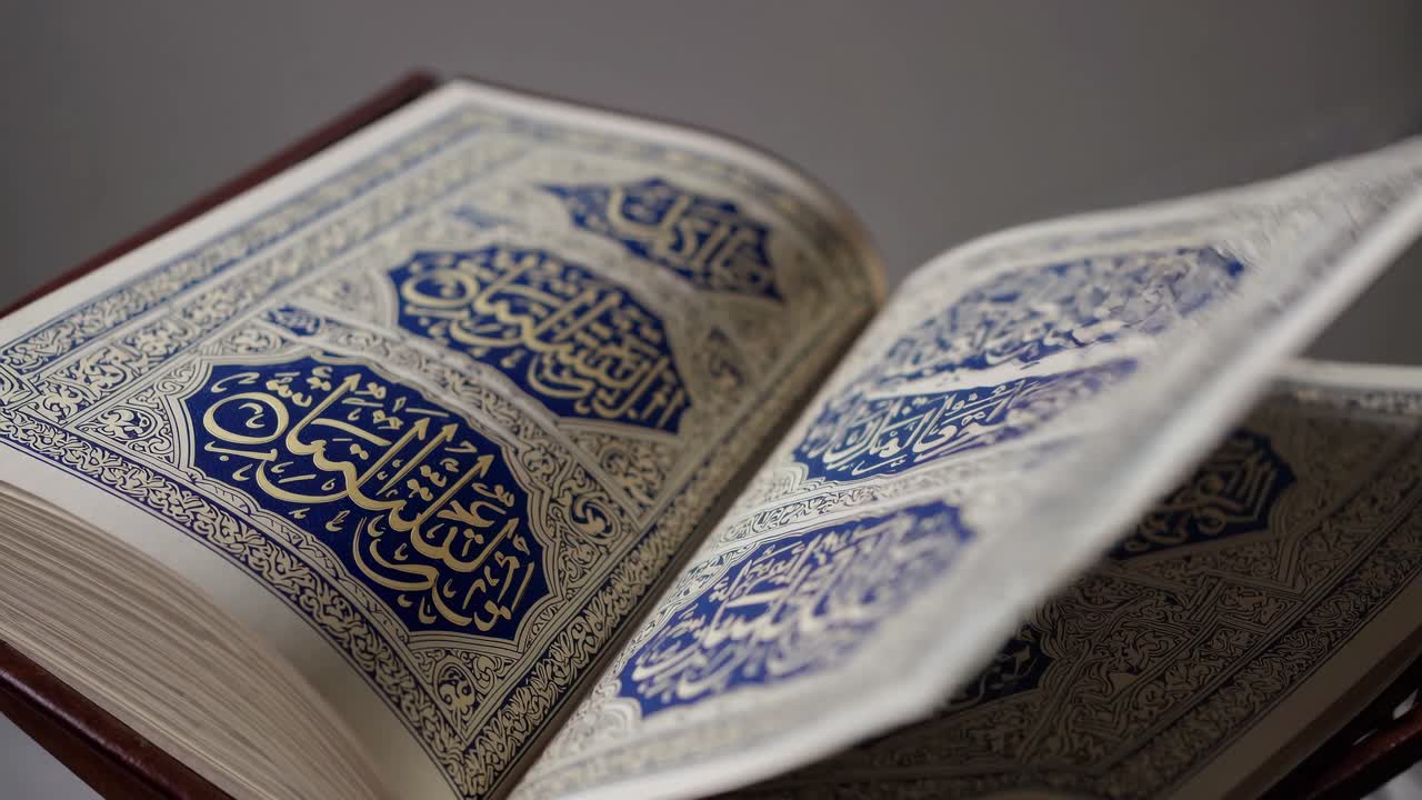 Video ravvicinato di un Corano aperto con calligrafia araba blu e oro.