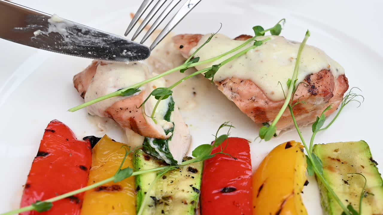 Close up of a woman eating a piece of chicken with white sauce and grilled vegetables at a restaurant