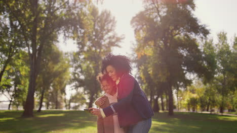 happy mom holding smartphone making funny selfie with cute daughter in park.