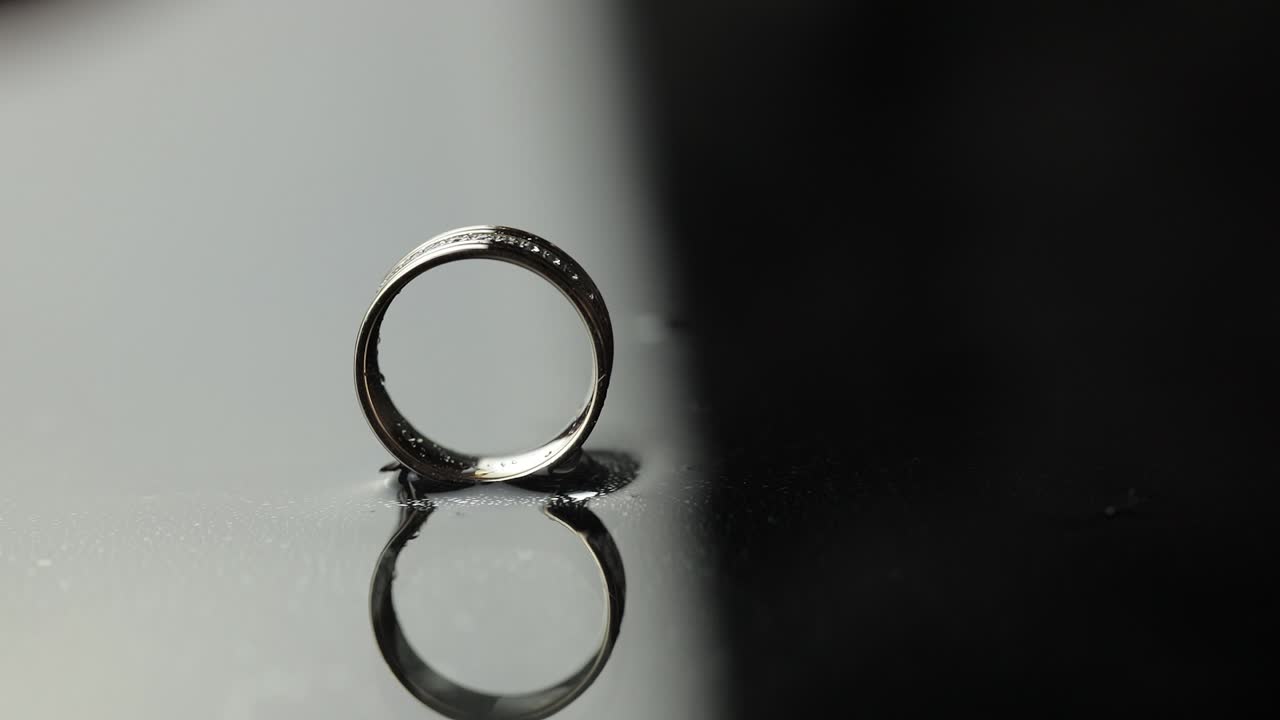 Wedding rings on black, white water surface. Groom ring rolling to bride's ring