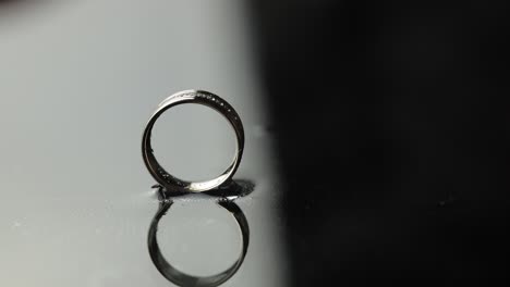 wedding rings on black, white water surface. groom ring rolling to bride's ring