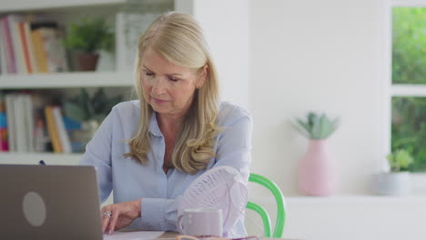 menopausal mature woman having hot flush at home cooling herself with fan connected to laptop