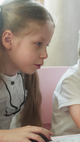smiling girl turns on cartoons on laptop to bored brother at table in children room. little children watch educative videos via computer at home