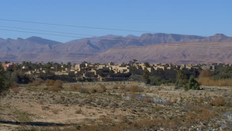 Slowly-panning-shot-of-a-Moroccan-desert-village-to-a-backdrop-of-high-mountains-on-a-sunny-day