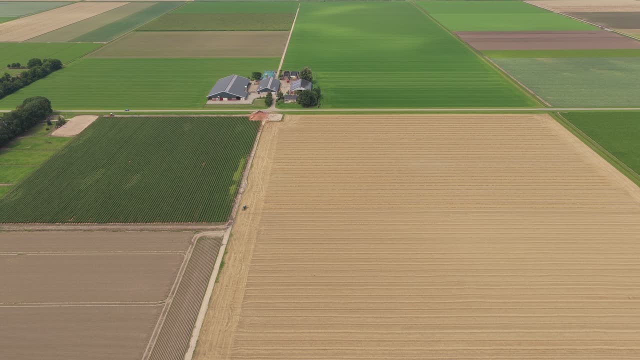 Traktor kultiverer landbrugsmark, landbrugsbygninger i baggrunden, Holland