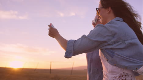 beautiful girl friends taking selfies on road trip at sunset with vintage car