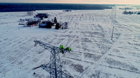 engineers working high on the power lines of an electric transmission tower in the winter countryside - aerial parallax