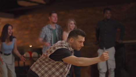 Portrait-A-young-Caucasian-man-makes-the-final-throw-with-a-bowling-ball-and-wins-the-game-with-the-support-and-joy-of-his-friends-of-different-nationalities.-Rejoice-and-celebrate-the-victory