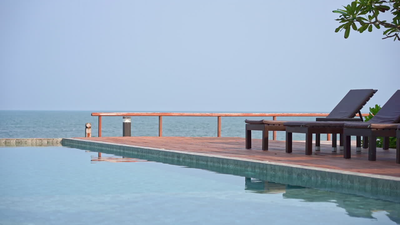 Peaceful poolside lounge chairs beside warm clear swimming pool with view of blue ocean in the distance. Horizon over water and scene of luxury tropical island resort in morning with no people
