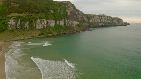 tilting up shot of cliffs along the coastline in new zealand with waves hitting the beach during the day