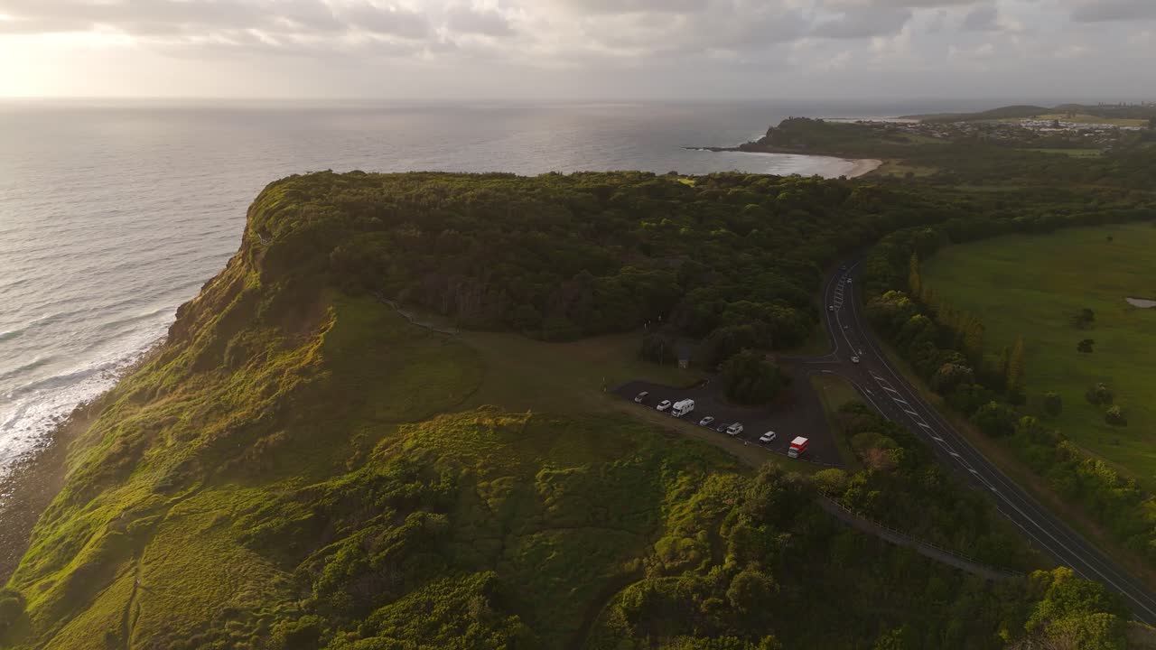 Sunset at coastline of Australia with driving cars. Aerial orbit wide shot. Ocean sea with green idyllic hills along island.
