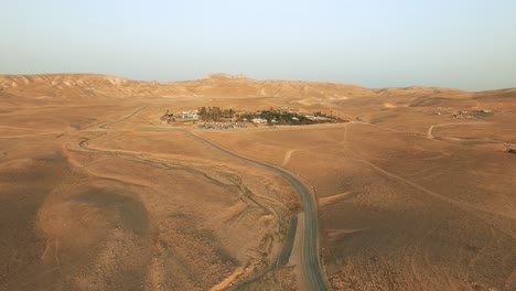 Aerial-view-of-a-green-oasis-of-trees,-farm-fields-at-the-edge-of-the-desert-with-Mountains-around