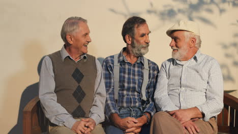Three-Senior-Men-Resting-On-A-Bench-And-Smiling-To-The-Camera-At-The-Wall