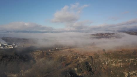 Vista-Aérea-De-La-Niebla-Fina-Sobre-La-Tierra-Rural-Fuera-De-La-Pequeña-Ciudad,-Tiro-De-Zoom