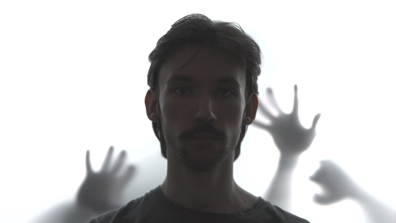 Uomo caucasico controluce con mani d'ombra che si protendono da un vetro smerigliato, motivo del paziente intrappolato, tensione e paura. Media