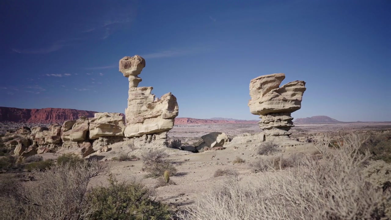 Amplia toma panorámica revela extrañas formaciones rocosas esculpidas por el viento en el Parque Provincial Ischigualasto bajo un cielo azul claro, destacando el paisaje desértico árido y la geología accidentada